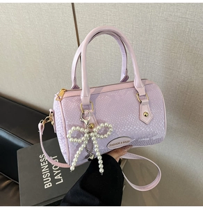 Close-up of a purple faux-snakeskin Boston bag featuring a pearl bow charm and metal logo