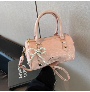 Close-up of pink snakeskin texture boston bag with pearl bow charm and dual handles