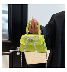 Detail of neon green mini handbag with a sparkling silver rhinestone bow and chain strap