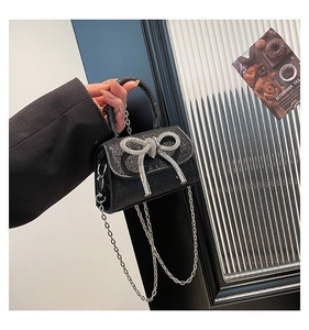 Close-up of mini black glitter handbag with rhinestone bow buckle and silver chain strap