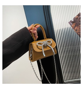 Detail of a ginger yellow mini handbag featuring a sparkly rhinestone bow and silver chain