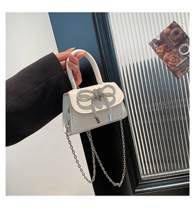 Detail view of white mini handbag featuring a crystal-encrusted bow and silver chain strap