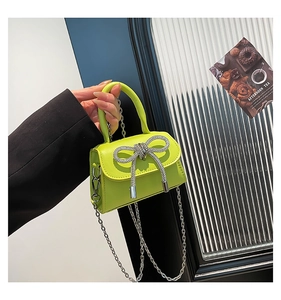 Detail of neon green mini handbag featuring a rhinestone bow and silver chain strap
