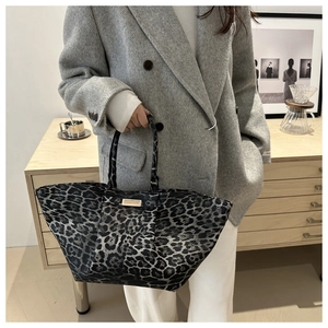 Detail of large leopard print tote bag featuring a gold metal plaque and long handles