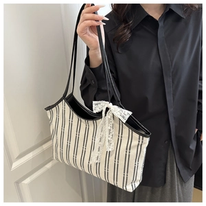 Detail of striped canvas tote bag featuring a white lace bow and black handle straps