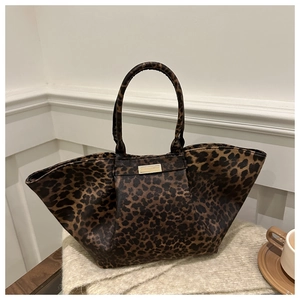 Close-up of leopard print tote bag with gold metal logo plate on soft beige blanket