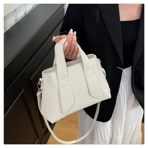 Detail of beige woven texture and silver hardware on a trapezoid commute handbag