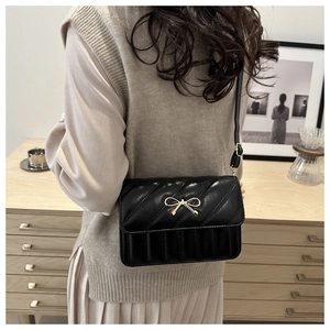 Sac bandoulière noir matelassé avec nœud doré porté par un mannequin en intérieur