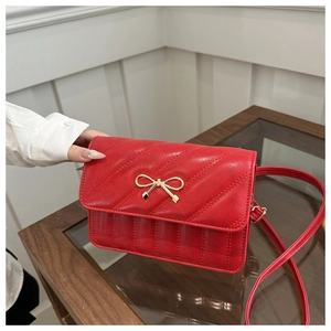 Detail of red quilted crossbody bag featuring a golden bow metal clasp and PU leather texture
