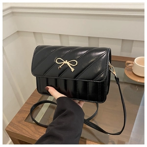Close-up of black quilted shoulder bag featuring a golden bow metal buckle detail