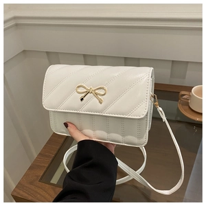 Close-up of white quilted mini crossbody bag with golden bow hardware on a cafe table