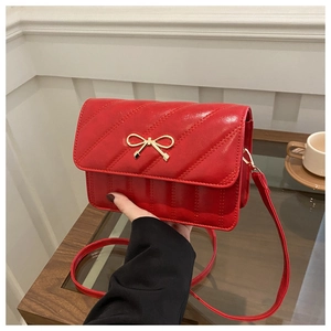 Close-up of red quilted leather handbag featuring a golden bow buckle and adjustable strap
