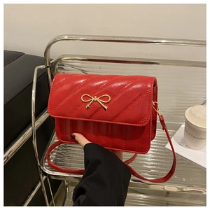 Détail d'un sac bandoulière rouge matelassé avec nœud doré et texture en cuir lisse