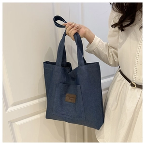 Détail du cabas en denim bleu avec écusson en cuir sur la poche avant porté par mannequin