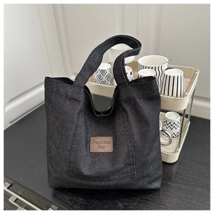Détail du sac cabas en denim noir avec étiquette en cuir brun et intérieur spacieux