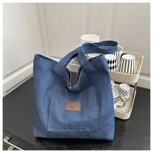 Gros plan du sac cabas en denim bleu foncé avec logo en cuir sur marbre noir