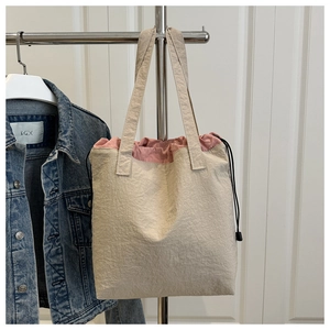 Detail of drawstring tote bag featuring beige textured fabric and pink trim accents