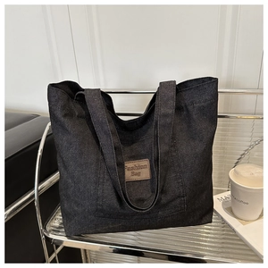 Détail d'un sac cabas en denim avec étiquette en cuir sur un support métallique