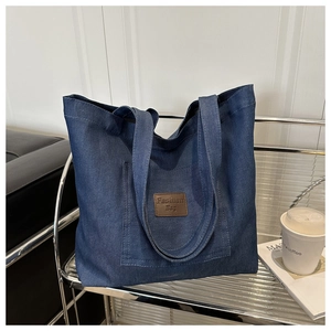 Détail d'un sac cabas en denim avec écusson en cuir et poche frontale pratique