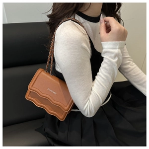 Brown leather crossbody bag with wave edges and silver chain strap shown on model
