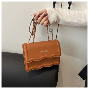 Detail of brown litchi pattern leather bag with wavy edge and metal chain strap