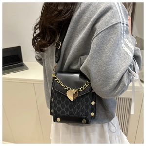 Detalle de bolso bandolera negro con estampado M y cadena dorada con dije de corazón