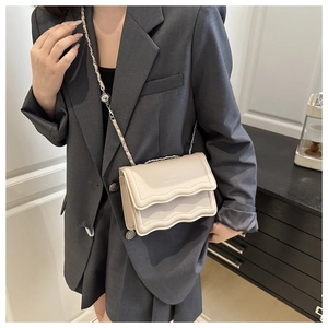 Detail of beige flap bag featuring wavy edges and chain strap on a grey suit jacket