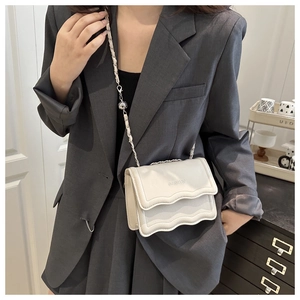 Detail view of white leather bag featuring scalloped flap design and silver chain strap