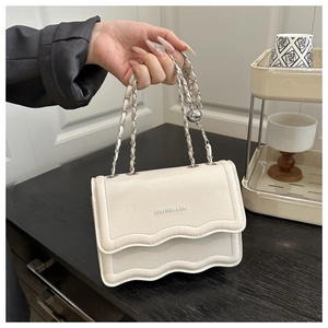 Close-up of white leather crossbody bag featuring wavy flap edges and chain strap