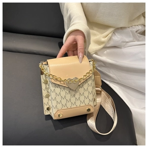 Detalle de mini bolso beige con monograma, cadena dorada de corazón y bandolera