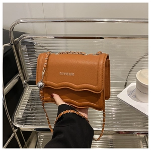 Detail of caramel small square bag featuring wavy edges and metallic ball charm on chain