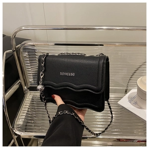 Detail of black leather crossbody bag with wavy edges and silver chain strap on shelf