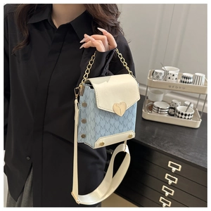 Detalle de bolso bandolera con estampado de monograma azul y cierre de corazón dorado