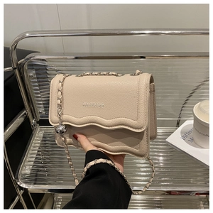 Detail of cream white leather bag showing wave-edge flap and silver chain strap