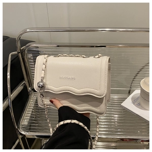 Close-up of white crossbody bag with wavy flap design and silver chain ball detail