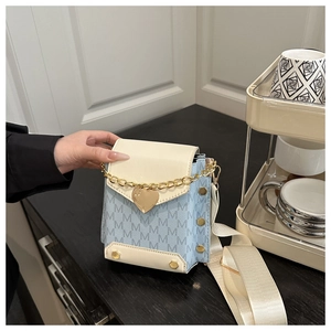 Detalle del bolso bandolera azul claro con estampado M, dije de corazón dorado y correa