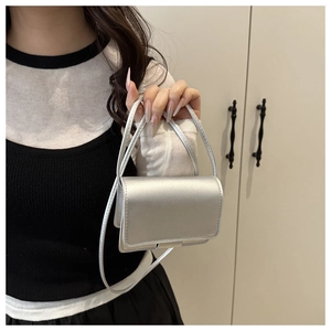 Detail of silver metallic square shoulder bag held by hand to show size and texture