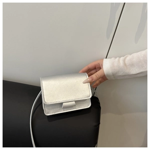 Mini silver metallic flap bag for girls held in hand showing compact size and fine strap