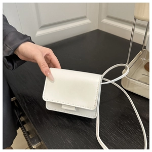 Detail of white mini leather flap bag showing smooth texture and slim shoulder strap