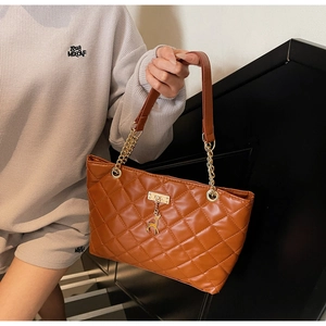 Detail of brown quilted tote bag featuring golden deer charm and metal chain strap