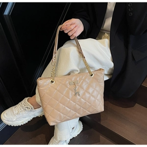Detail of beige quilted tote bag with gold deer pendant and metal chain shoulder strap