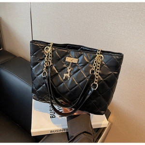 Detail of black quilted leather tote bag with gold chain and deer-shaped pendant