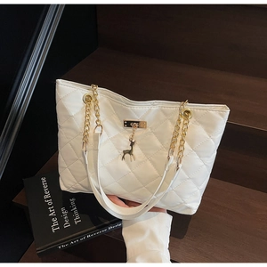 Close-up of white quilted tote bag featuring gold chain strap and deer-shaped metal pendant