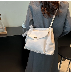 Close-up of minimalist cream white crossbody bag with lace bow and gold twist lock