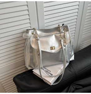 Detail of silver metallic tote bag featuring gold twist lock and white lace bow decor