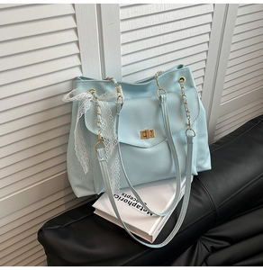 Detail of light blue tote bag featuring a gold twist lock and a white lace bow accent