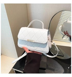 Detail view of a white quilted handbag with a gold metal lock and leather strap