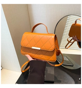 Detailed view of an orange quilted crossbody bag with golden metal hardware and top handle