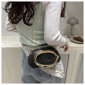 Detail of a chic black leather crossbody bag featuring a large gold oval buckle and chain