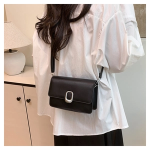 Detail view of black rectangular crossbody bag with silver buckle on minimalist outfit